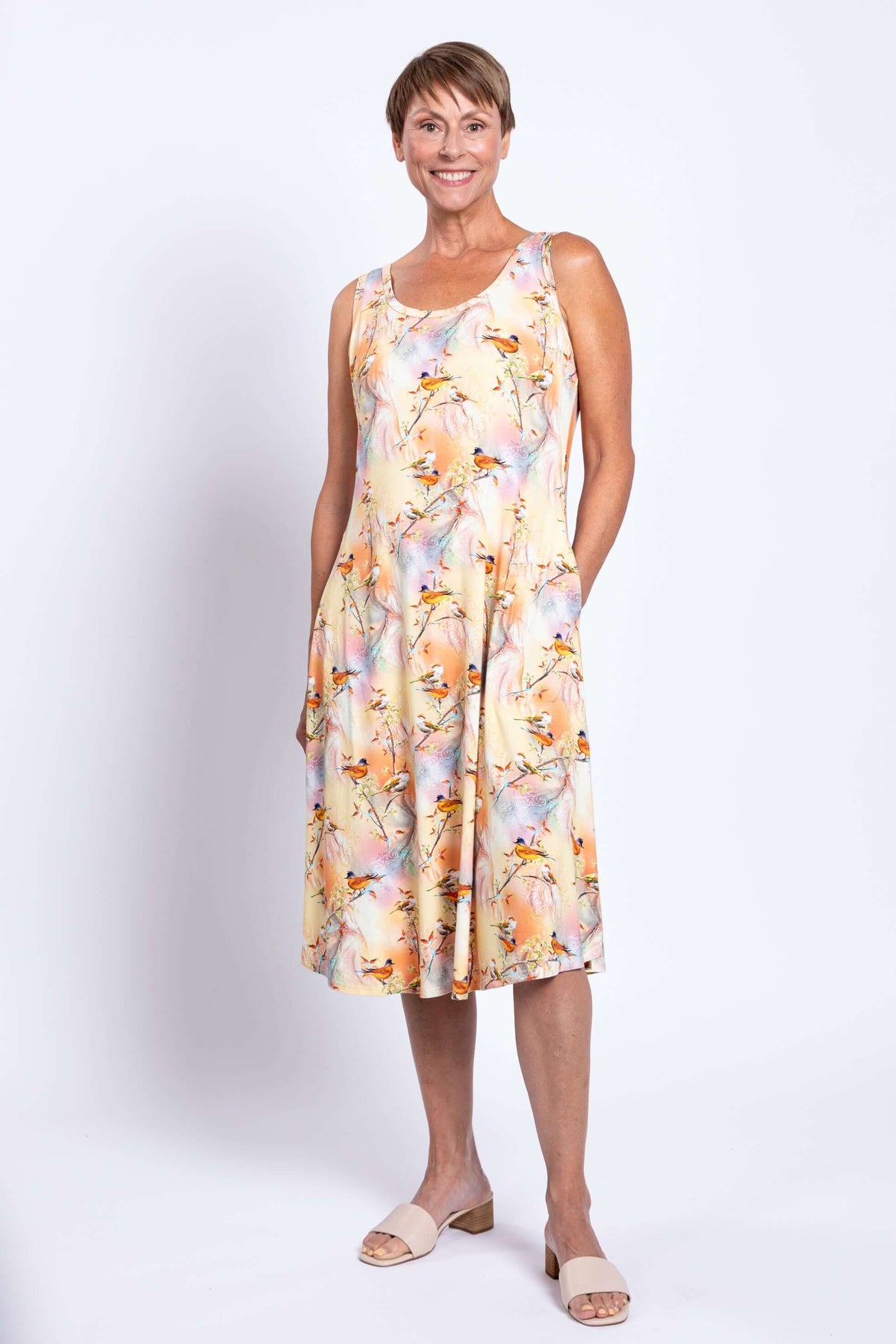 Woman standing in sleeveless pastel dress, smiling, with side pockets