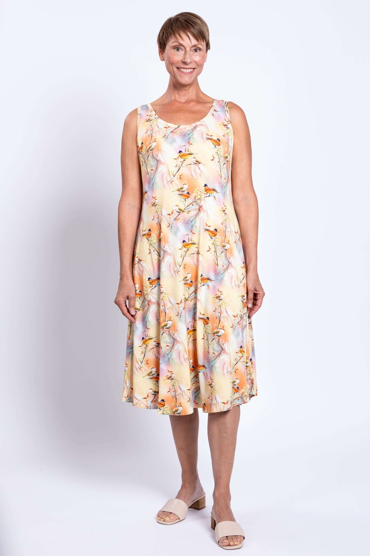 Front view of woman in sleeveless pastel dress with bird print and side pockets