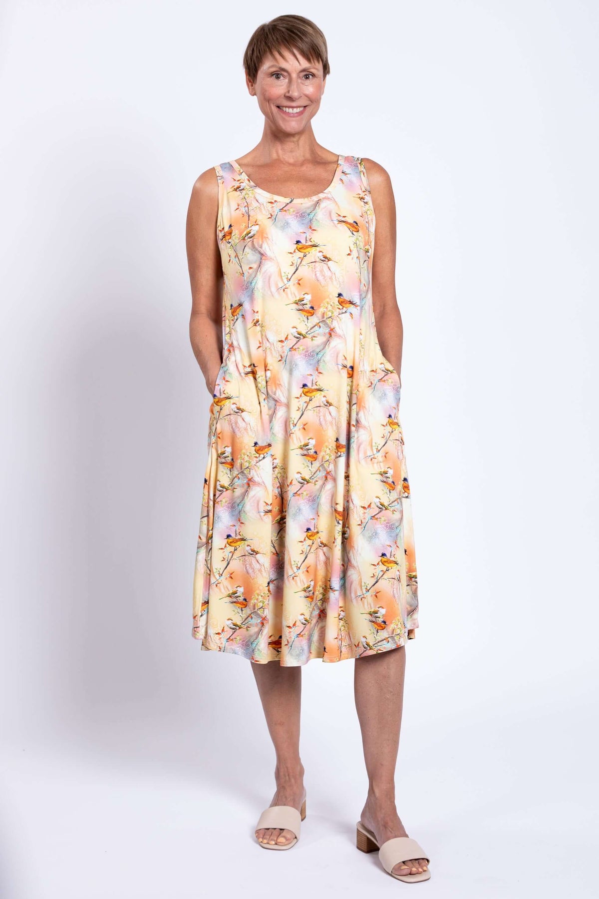 Woman wearing a sleeveless pastel-colored tank dress with bird print and side pockets