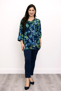 Woman wearing a blue and green floral top and navy pants against a white background, full body view