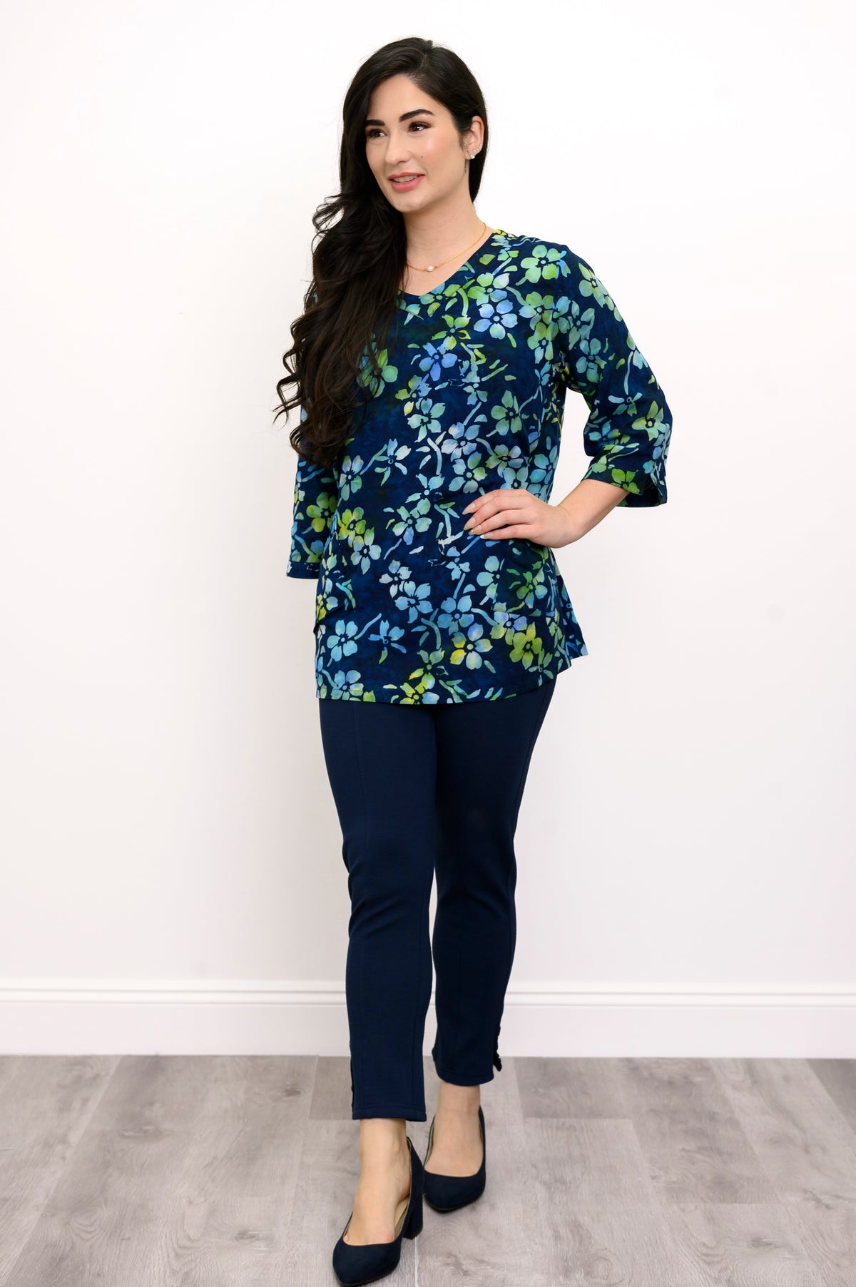 Woman wearing a blue and green floral top and navy pants against a white background, front view