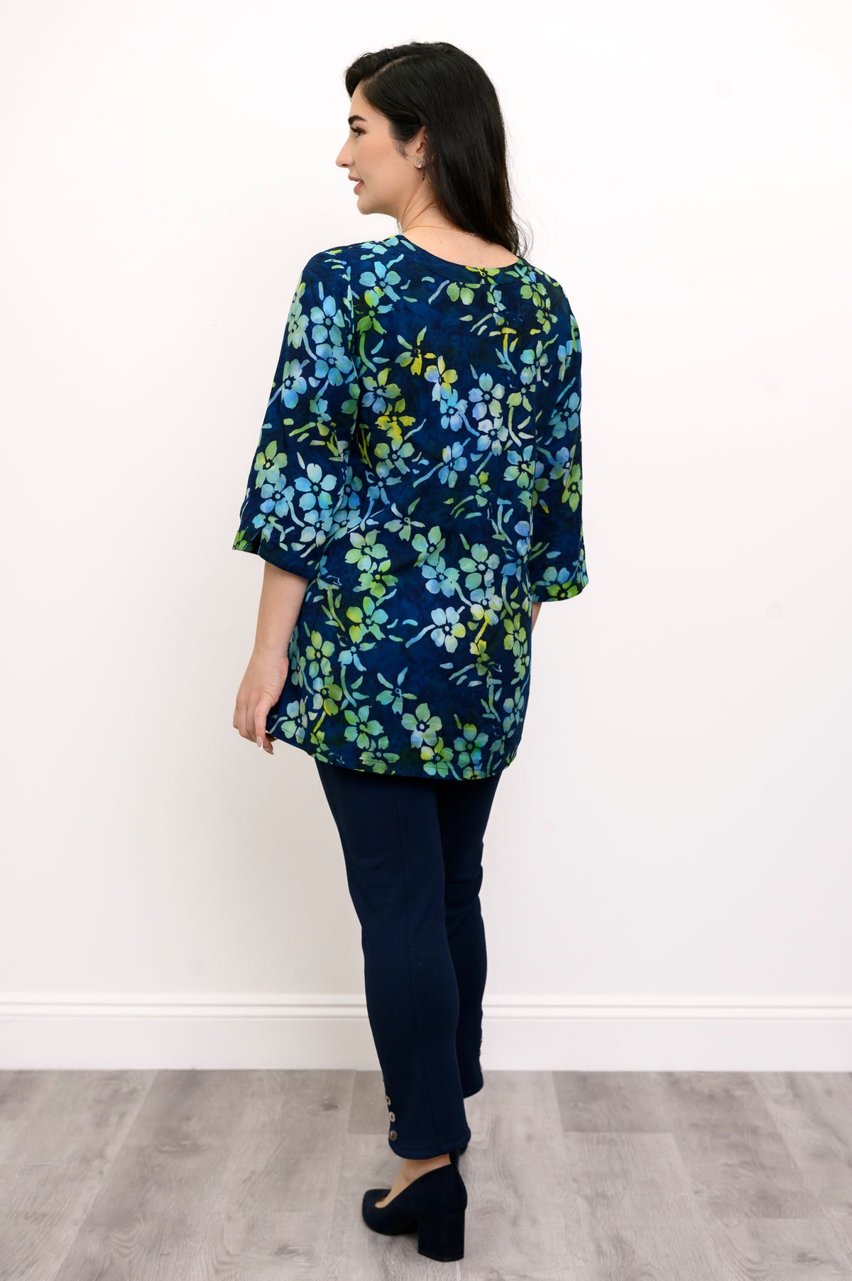 Woman wearing a blue and green floral top and navy pants against a white background, back view