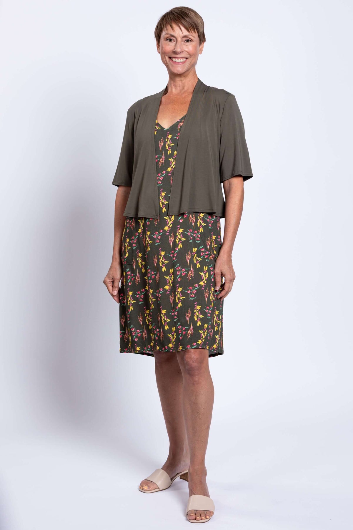 Woman in green floral dress with olive cardigan, full front view