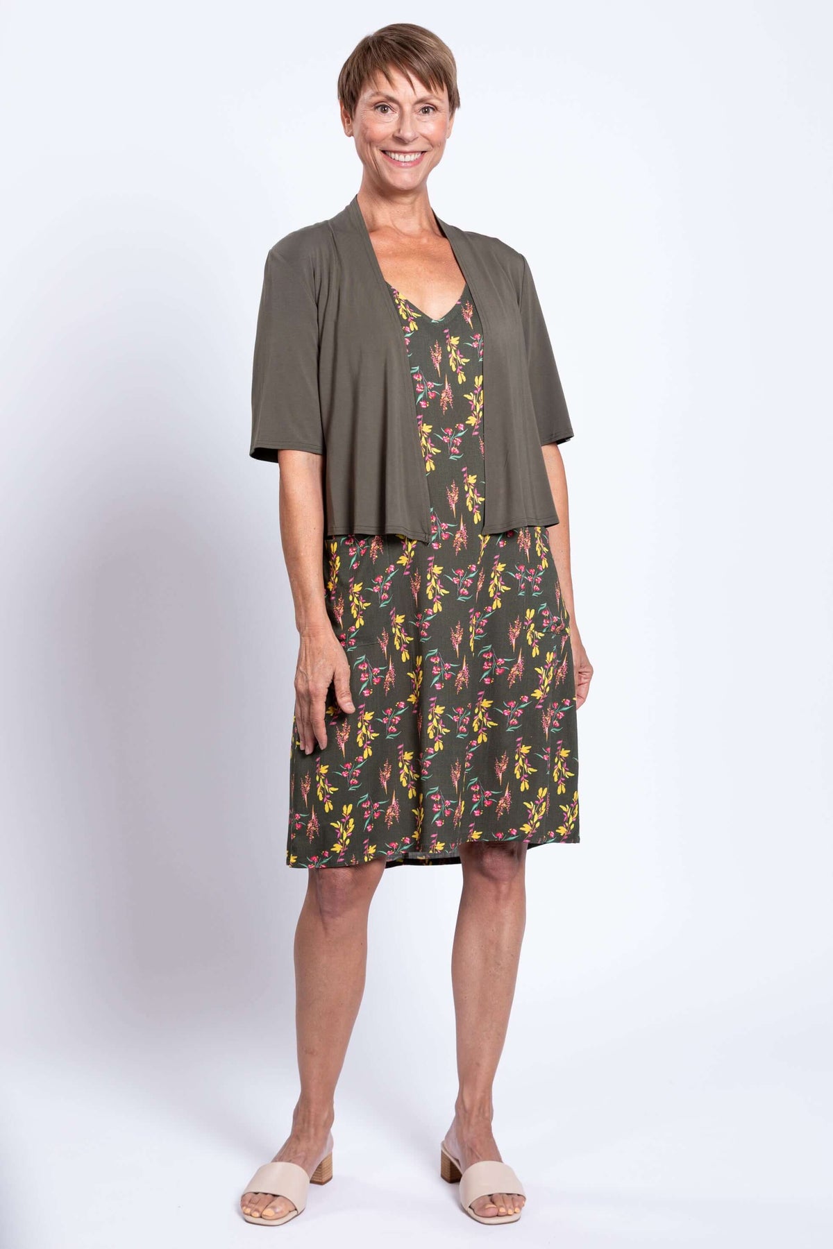 Woman in green floral dress with open olive cardigan, front view