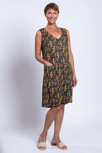 Woman in green floral sleeveless shift dress, hand in pocket, side front view