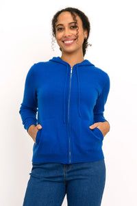 Close-up front view of woman smiling with her hands in the pockets of her cobalt blue knit hoodie