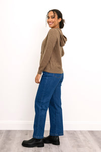 Woman wearing a knit brown hoodie with pockets and denim pants in front of a white background, side view