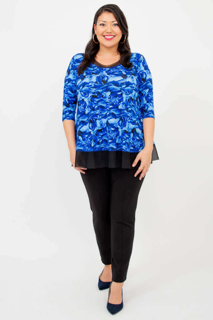 Full-length view of woman in blue floral top and black pants, facing forward