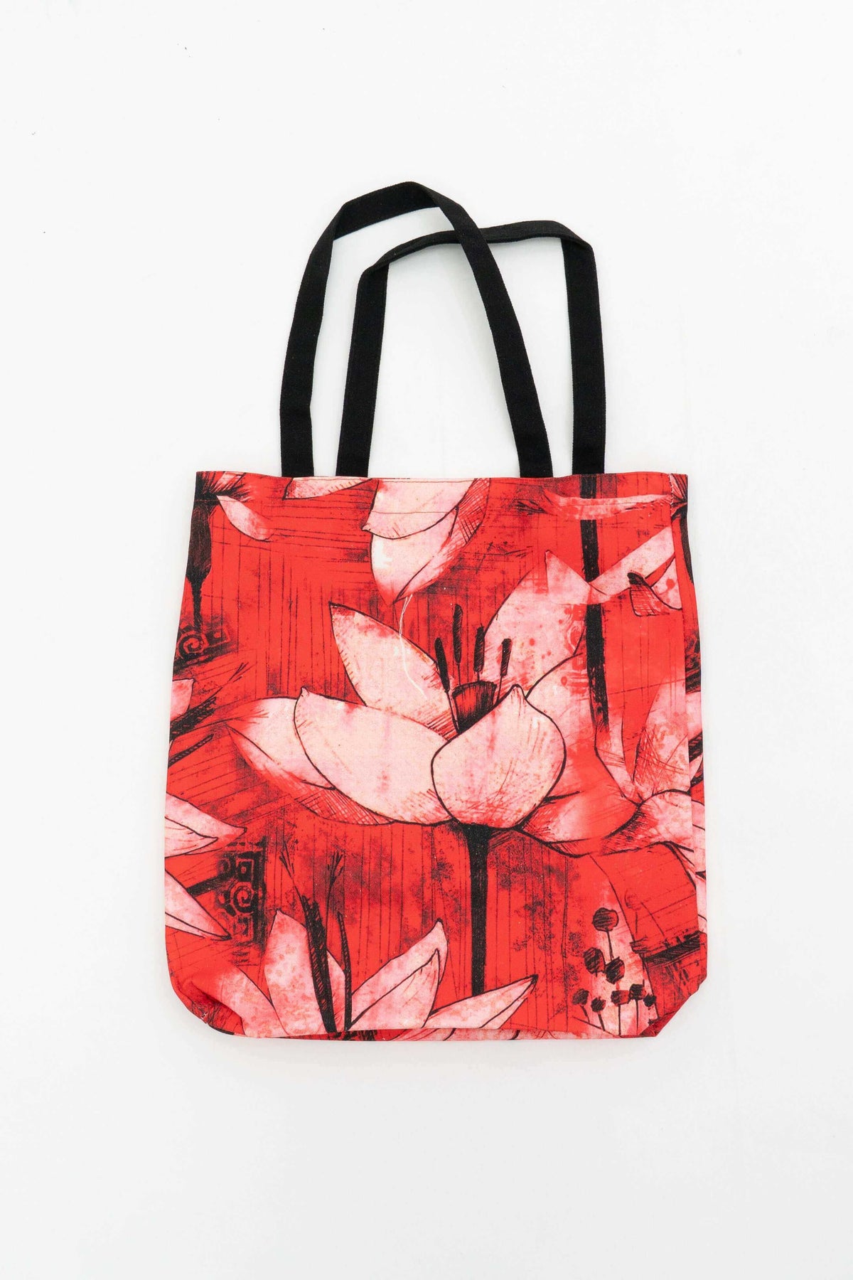 Red and pink floral print cotton canvas tote bag with black handles against a white background