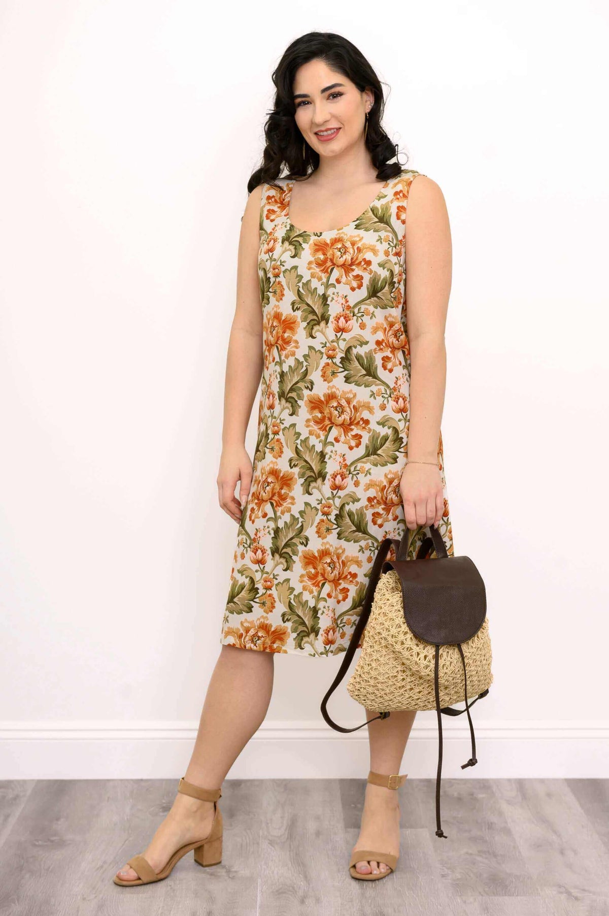 Woman in floral dress holding woven backpack, showing full outfit