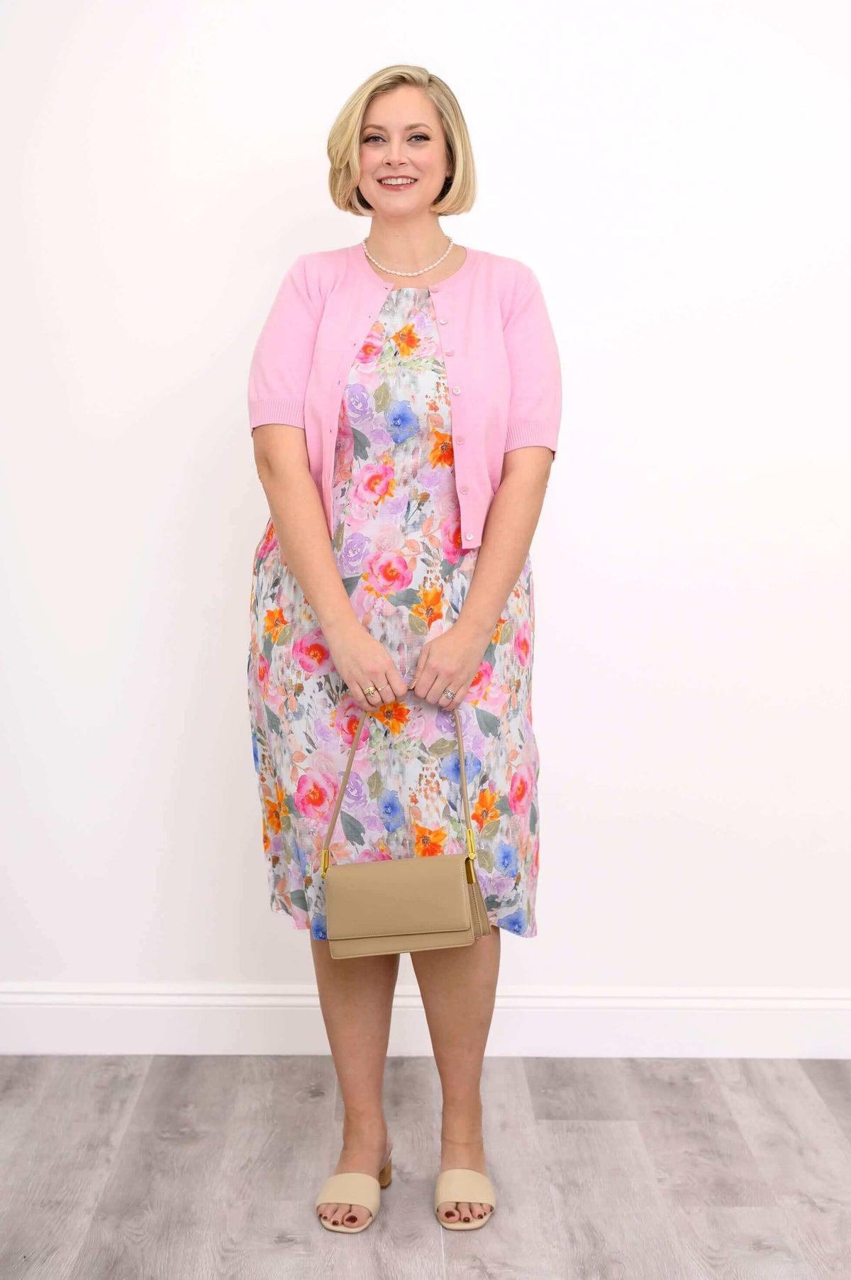 Woman in floral shift dress, pink cardigan, and beige heels with handbag