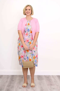 Woman in floral shift dress, pink cardigan, and beige heels with handbag