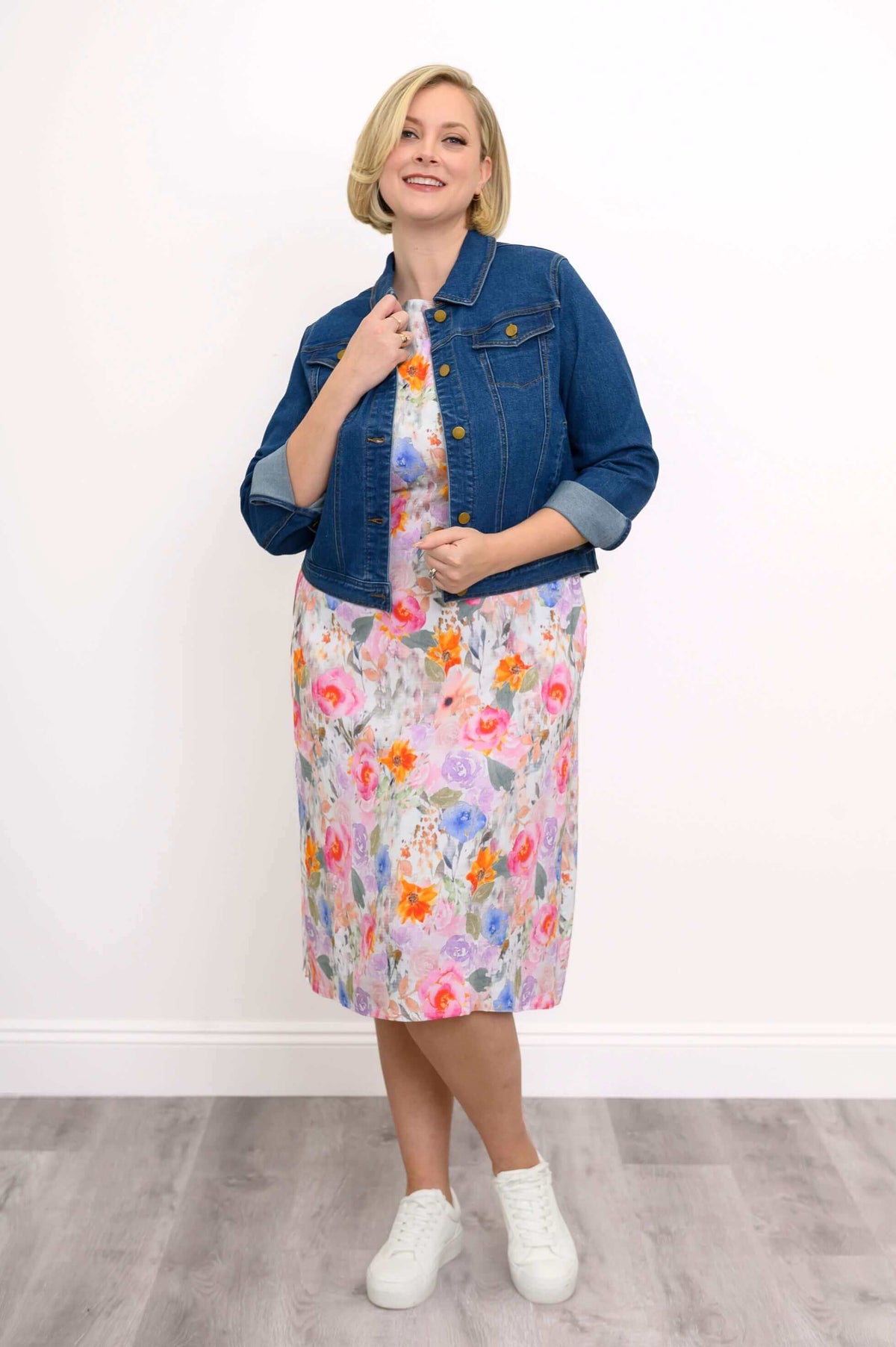 Woman styling floral shift dress with a classic denim jacket and white sneakers