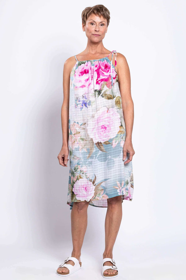 Woman modeling a floral summer dress with tie strap, standing against white background