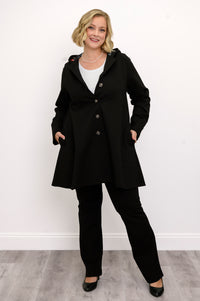 Woman modeling a black hooded A-line coat with button closure standing on a white background.