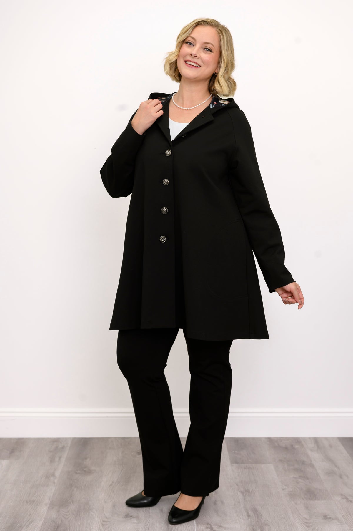 Full length front view of a woman wearing a black modal A-line coat paired with black trousers.