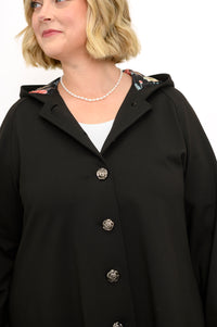 Close up view of a woman wearing a black modal button down coat styled with a pearl necklace.