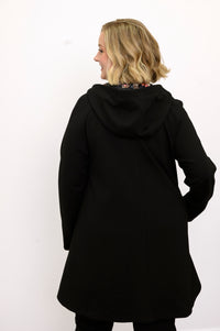 Rear profile shot of a long sleeve black swing coat displaying fluid drape and hooded back seam.