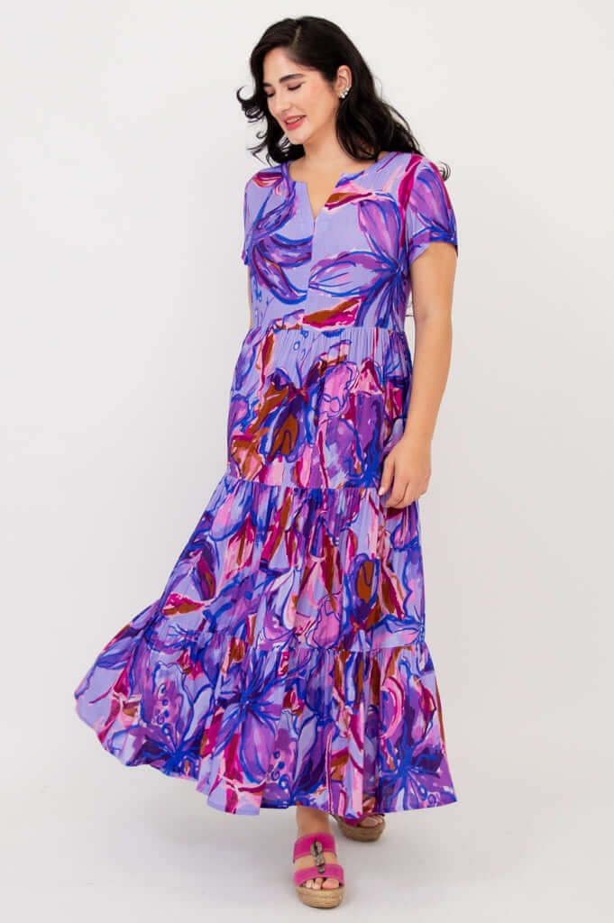 Woman in a flowing purple floral maxi dress with short sleeves, side pose showing movement
