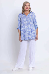 Full body shot of woman in flowy blue floral shirt and white pants