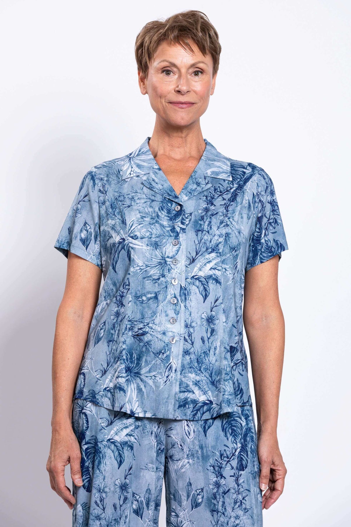 Woman wearing a blue floral short-sleeve button-up shirt and pants, facing forward