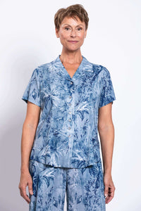 Woman wearing a blue floral short-sleeve button-up shirt and pants, facing forward