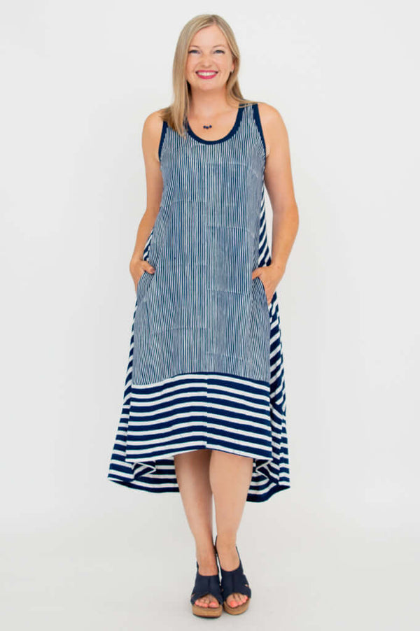 Front view of a woman wearing a sleeveless navy and white striped hi-lo dress with pockets