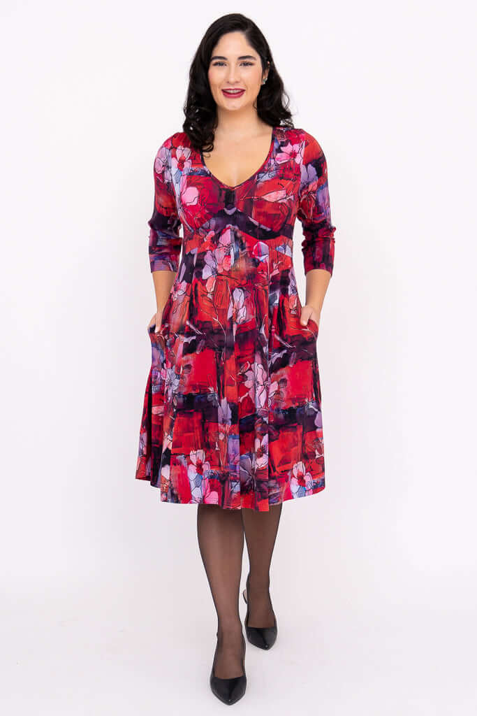 Front view of woman with hands in pockets wearing a red and purple floral fit and flare dress