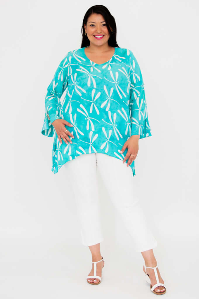 Smiling woman in turquoise printed top with shark-bite hem, standing and posing, front angle