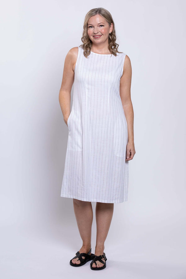 Woman in a white sleeveless striped midi dress with hands in pockets, front angle
