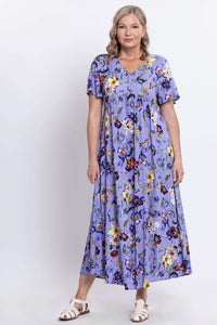 Front view of a woman in a long flowing lavender dress with a colorful floral pattern