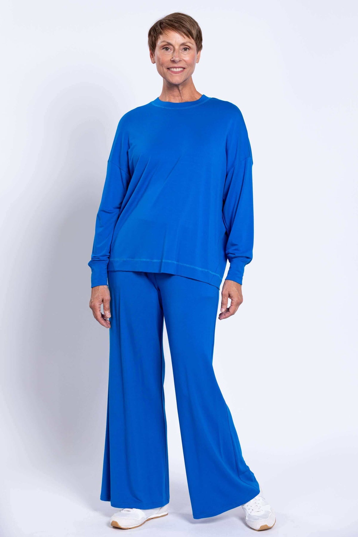 Woman modeling a loose-fitting blue bamboo top with flared blue pants from the front