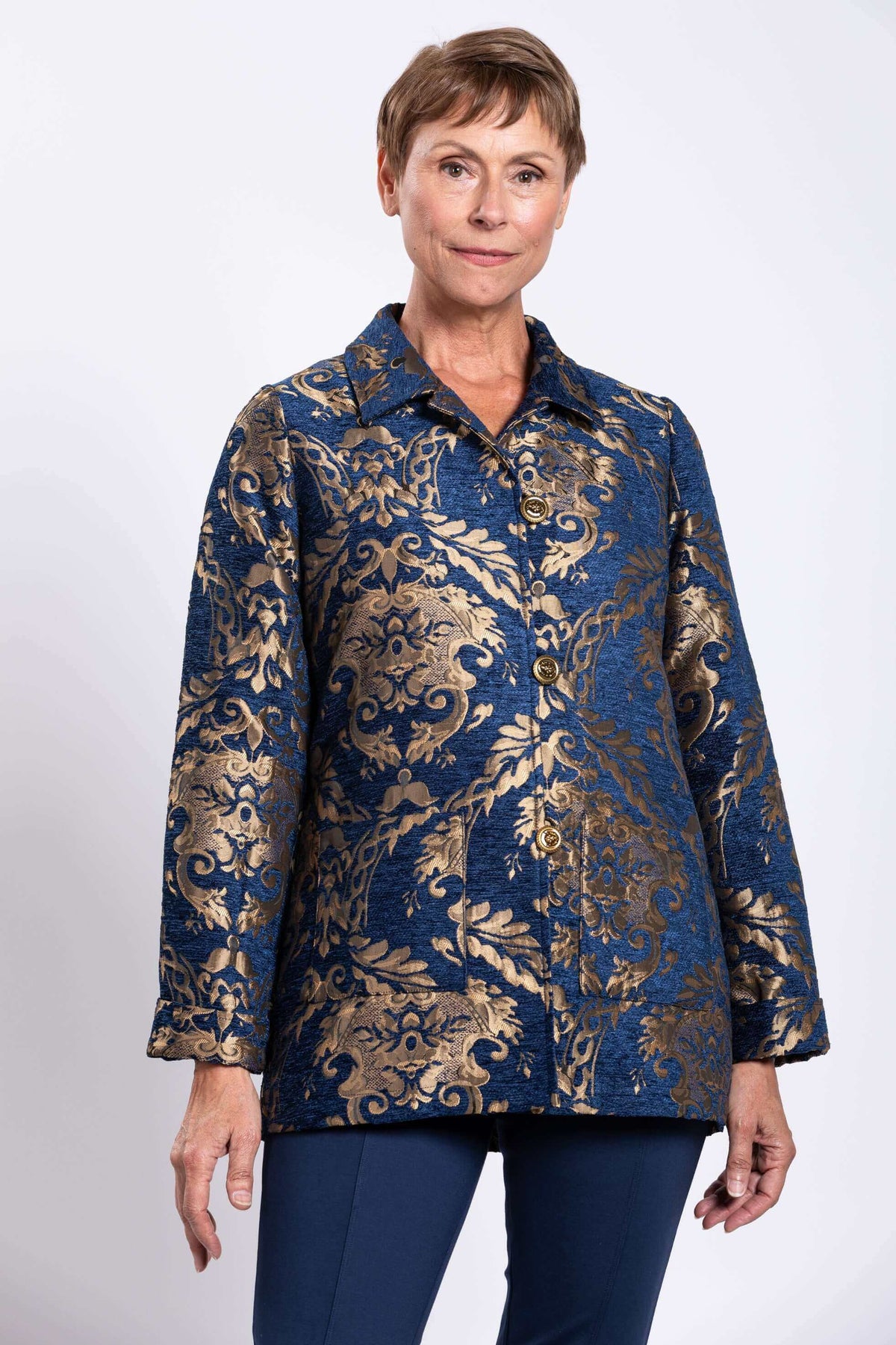 Front view of a woman wearing a short navy and gold jacquard coat with brass buttons