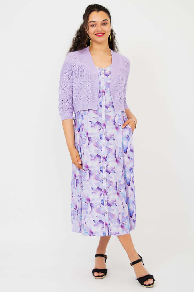 Front view of woman posing in lilac cropped cardigan and purple patterned dress