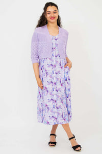 Front view of woman posing in lilac cropped cardigan and purple patterned dress