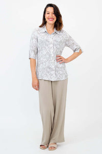 Front view of a woman posing in a patterned blouse with neutral colored wide-leg pants and sandals