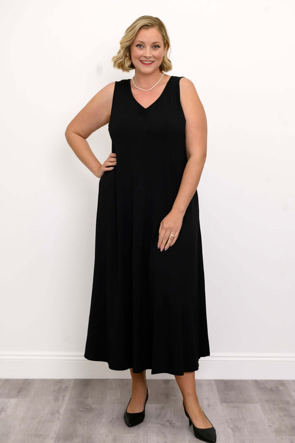 Woman posing in a black ruched V-neck maxi dress, hand on hip, smiling