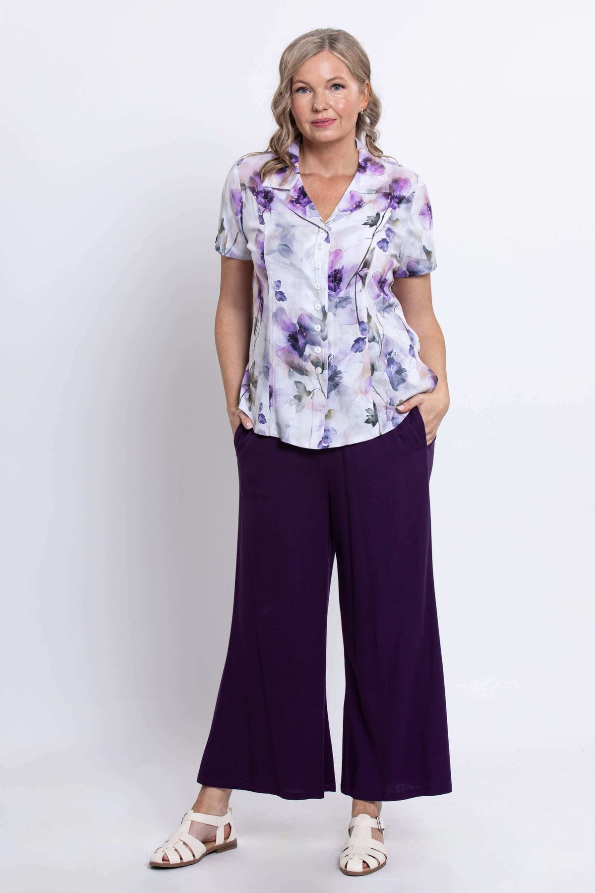 Front three-quarter view of a woman in a floral button-up shirt and purple pants