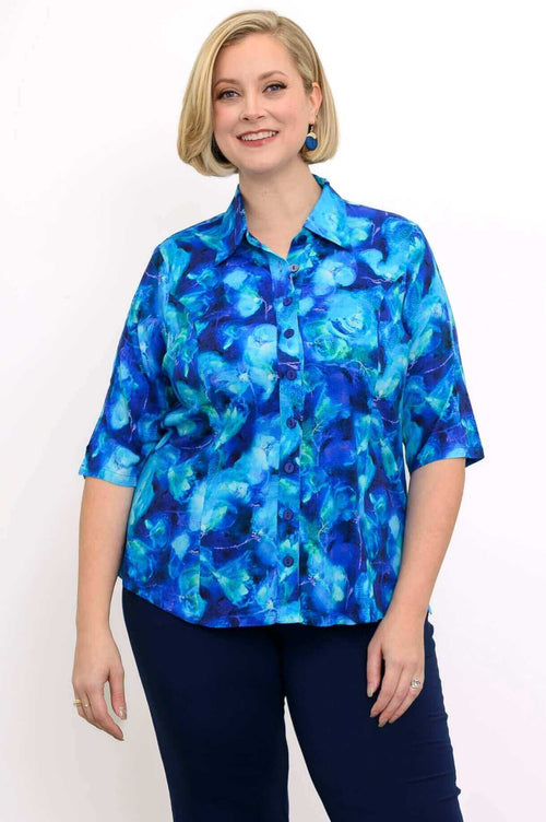 Front view of woman wearing blue patterned button up blouse and dark blue pants