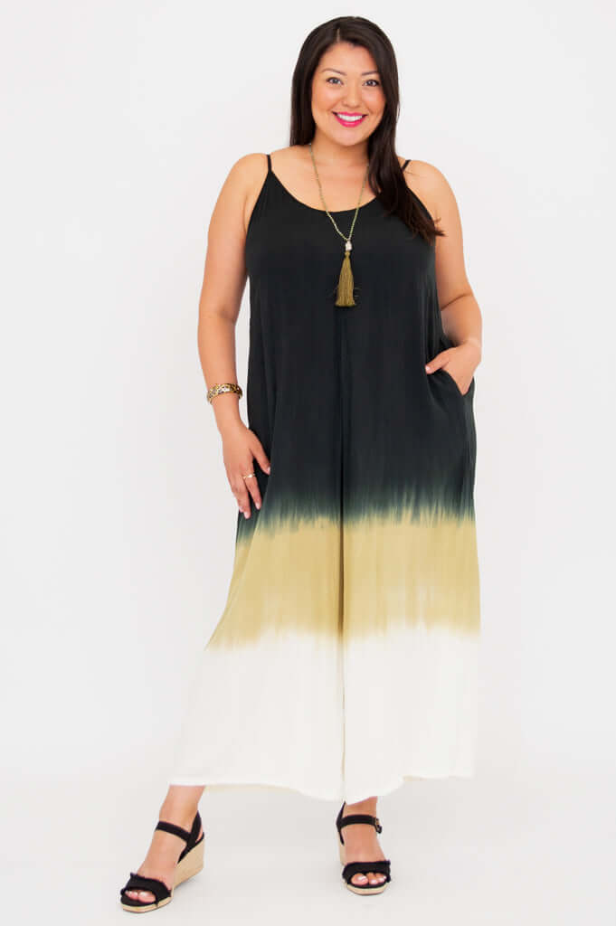 Front view of a woman wearing a black, olive, and ivory ombre jumpsuit with adjustable straps