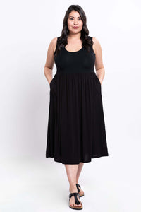 Front view of model in black sleeveless empire waist midi dress with hands in pockets