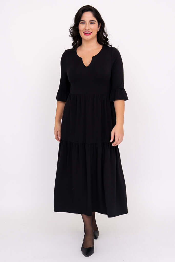 Front view of woman wearing a black tiered midi dress with keyhole neckline and ruffle sleeves