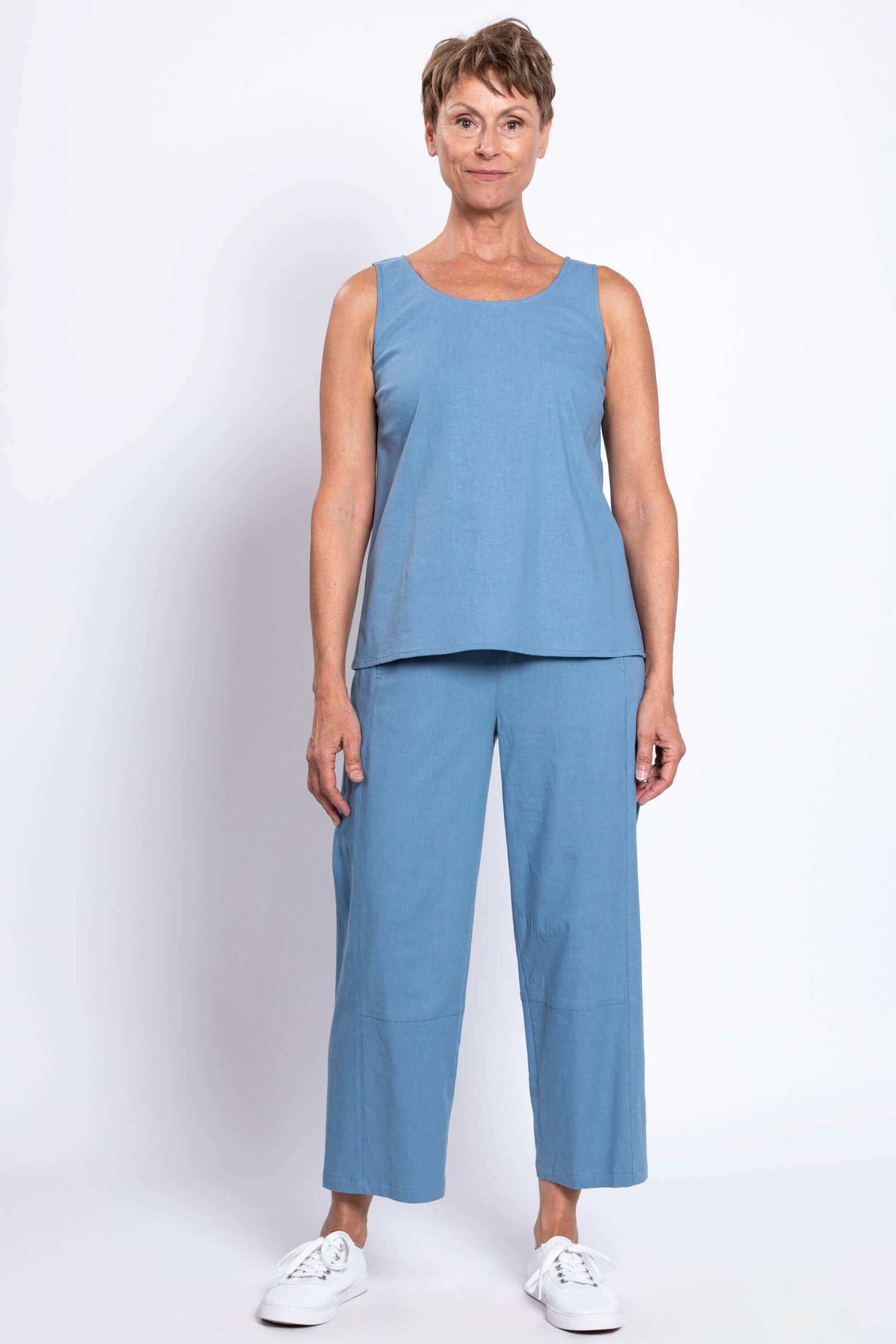 Woman in blue sleeveless top and cropped blue pants, standing straight, facing front
