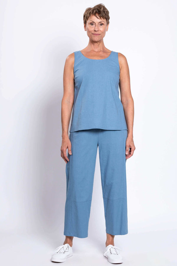 Woman in blue sleeveless top and cropped blue pants, standing straight, facing front