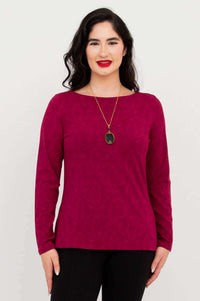 Woman wearing a berry long sleeve top and black pants, facing forward