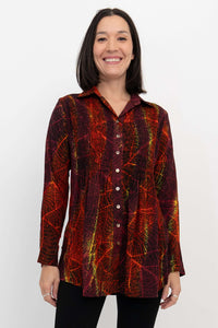 Woman wearing a long sleeve button-up tunic with vivid red and yellow leaf pattern