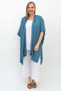 Woman wearing an ocean blue Darcy kimono wrap over white top and pants, front view