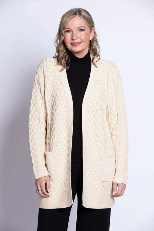 Front view of a woman wearing a cream cable knit open front cardigan with patch pockets