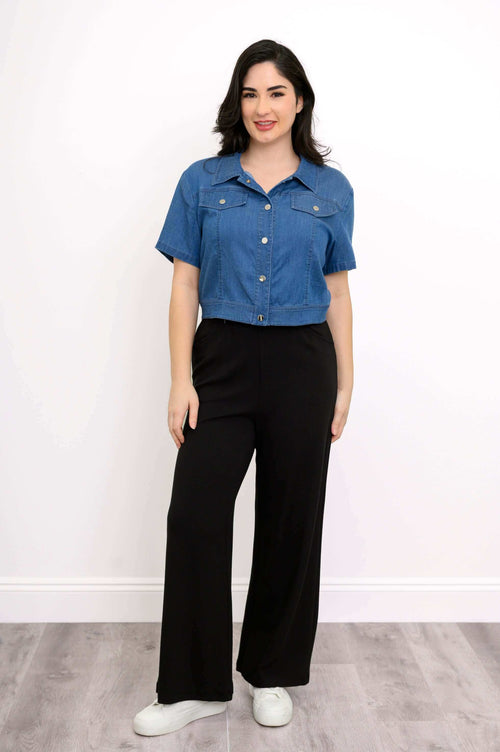 Front view of model wearing a cropped blue denim jacket with short sleeves and black pants