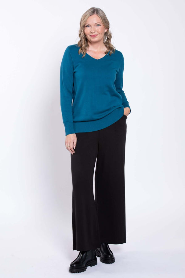 Front view of a woman wearing wide-leg black pants and a teal sweater